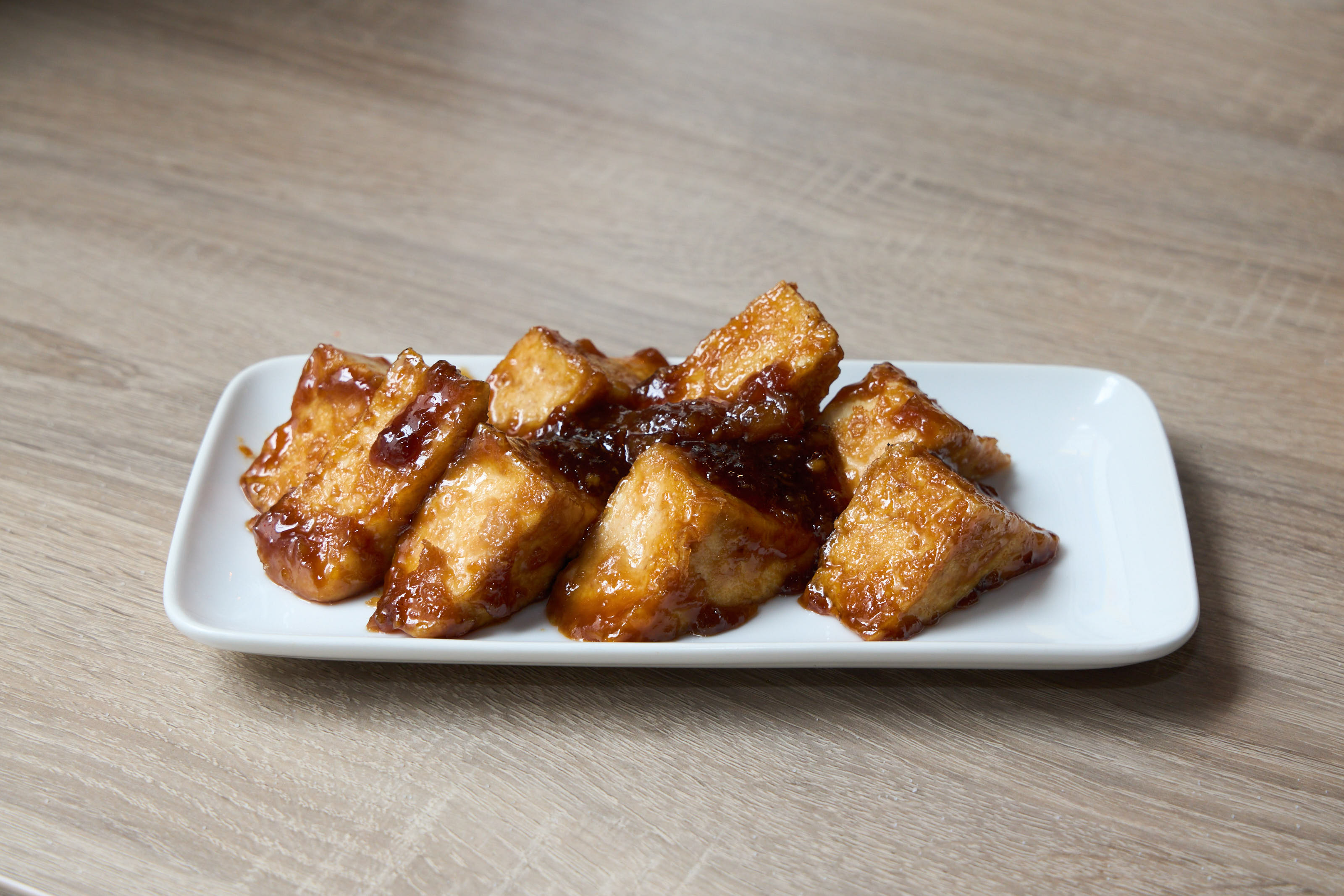 Crispy tofu steak pieces with teriyaki garlic glaze on white plate