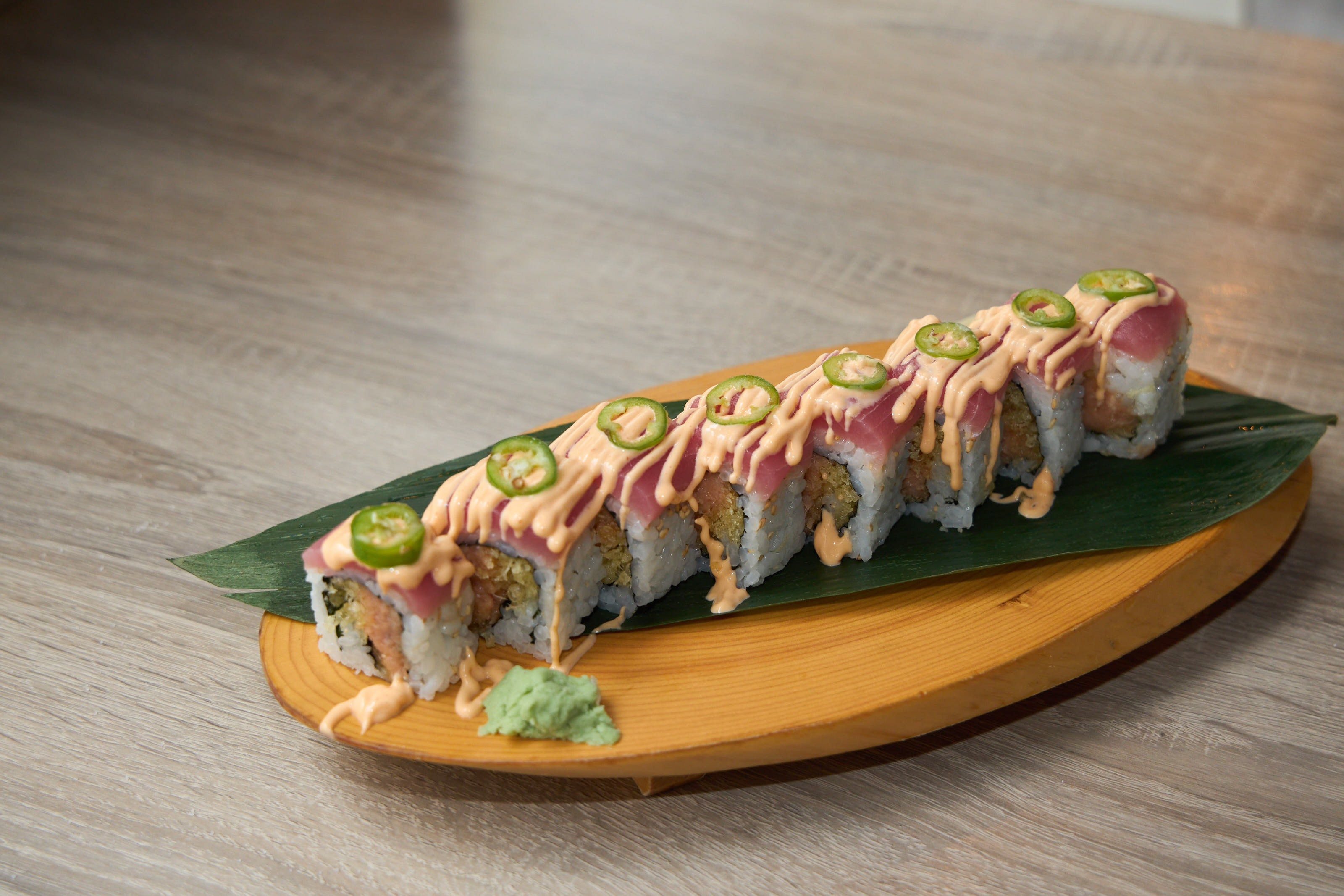 Jalapeño tuna roll with tuna cap, jalapeño slices and spicy mayo on wooden boat