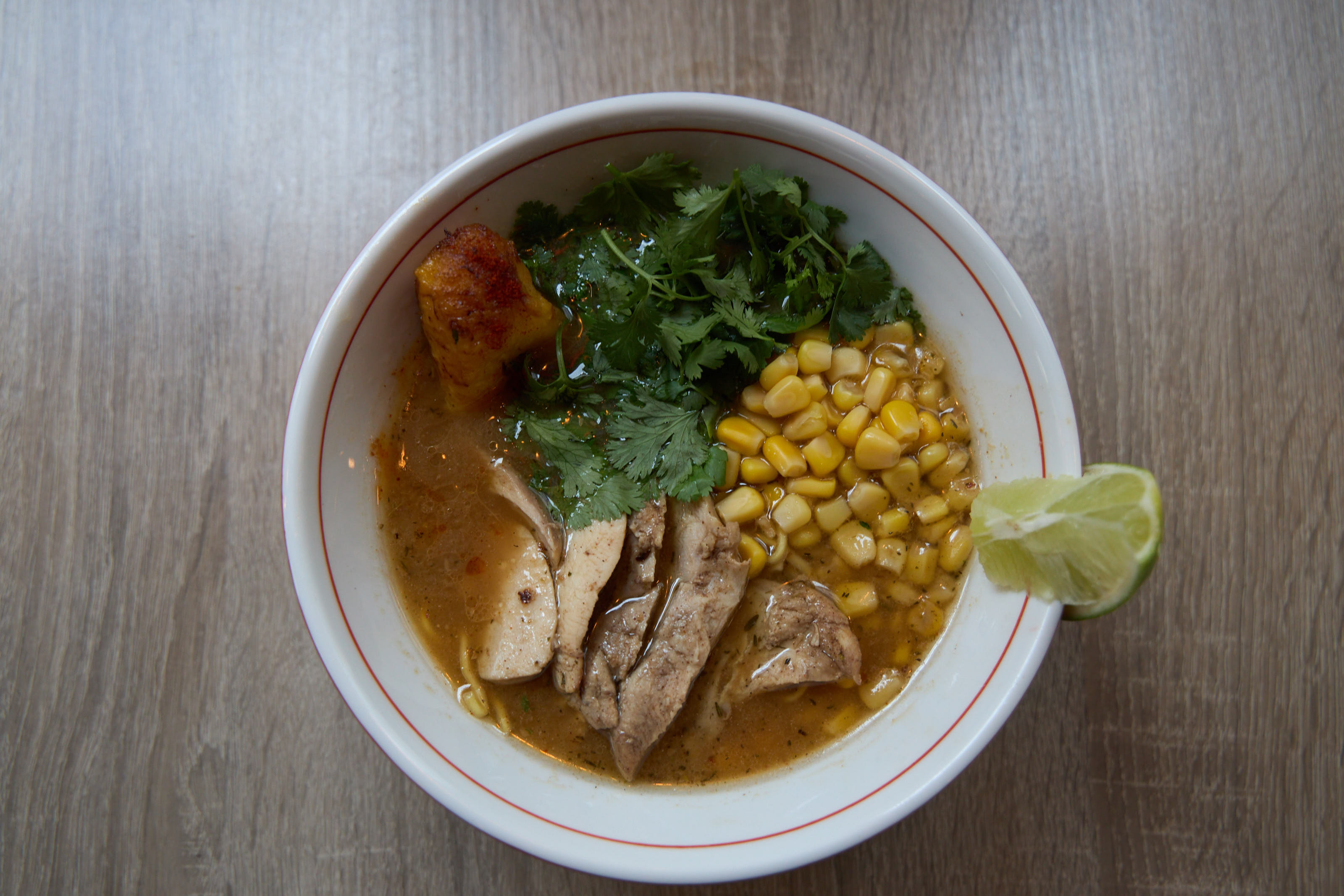 Chicken ramen with corn, cilantro, and lime in white bowl