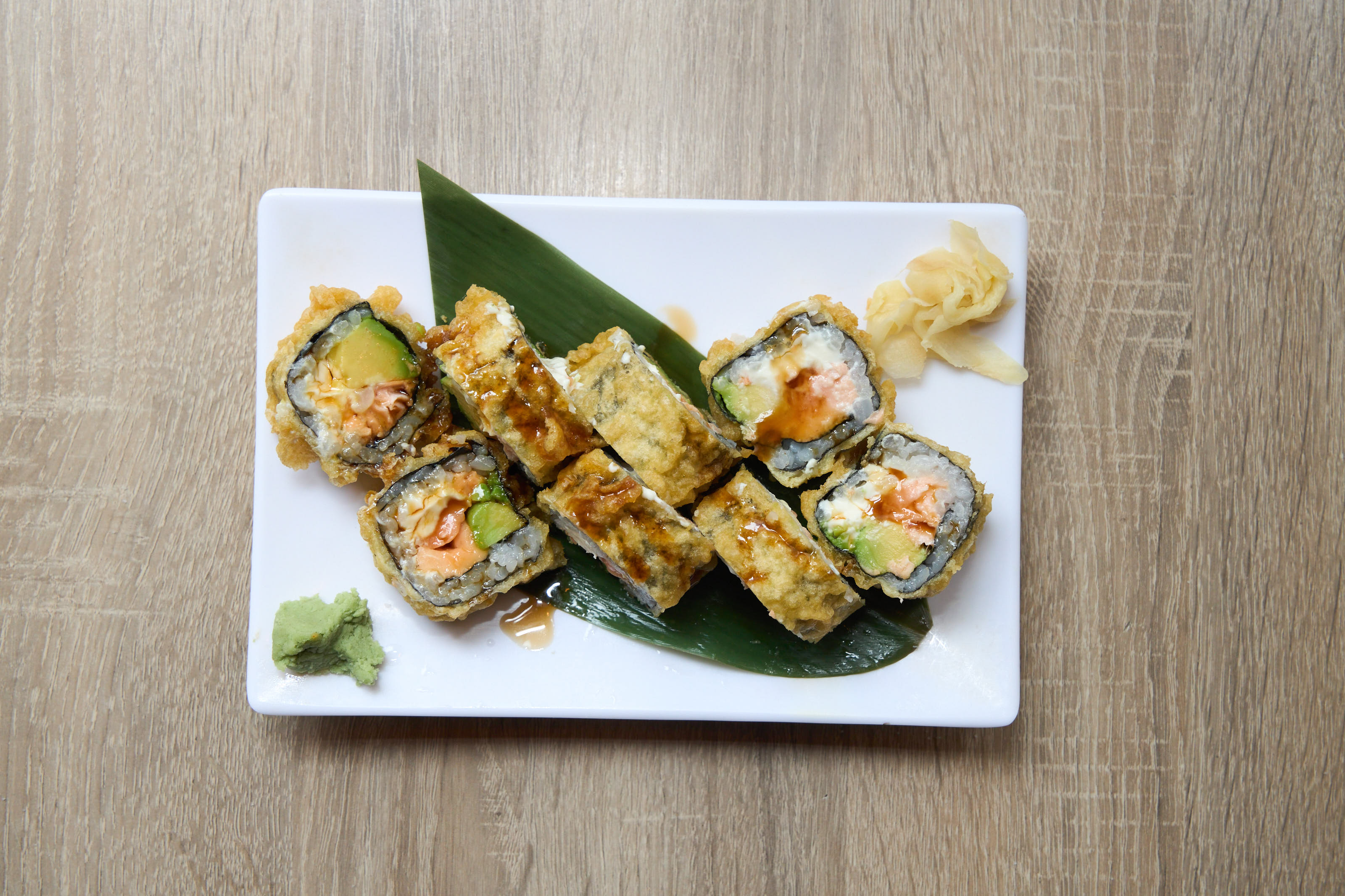 Crispy crunchy tempura roll pieces overhead on white plate with banana leaf