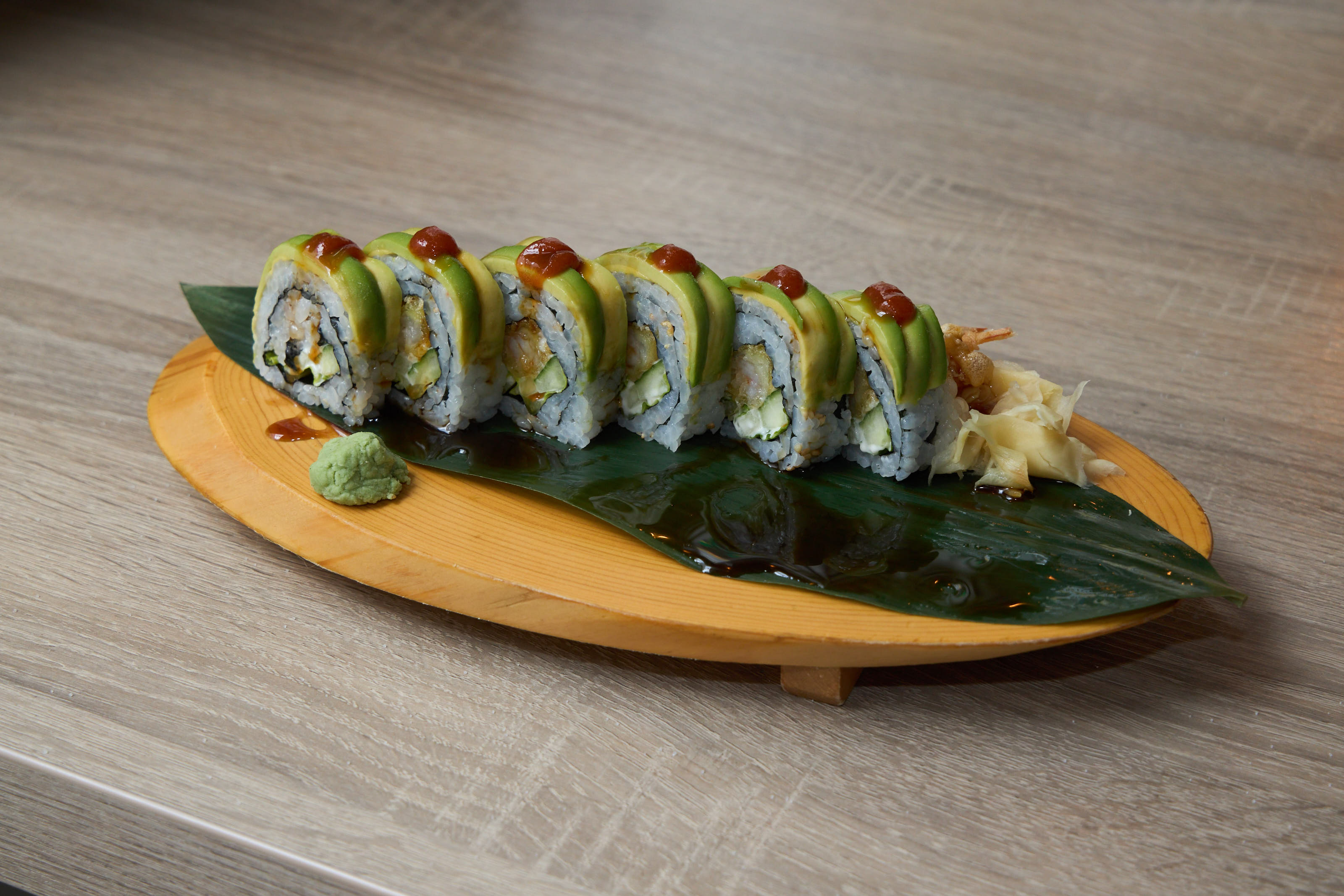 Dragon roll with avocado cap and spicy sauce on wooden boat