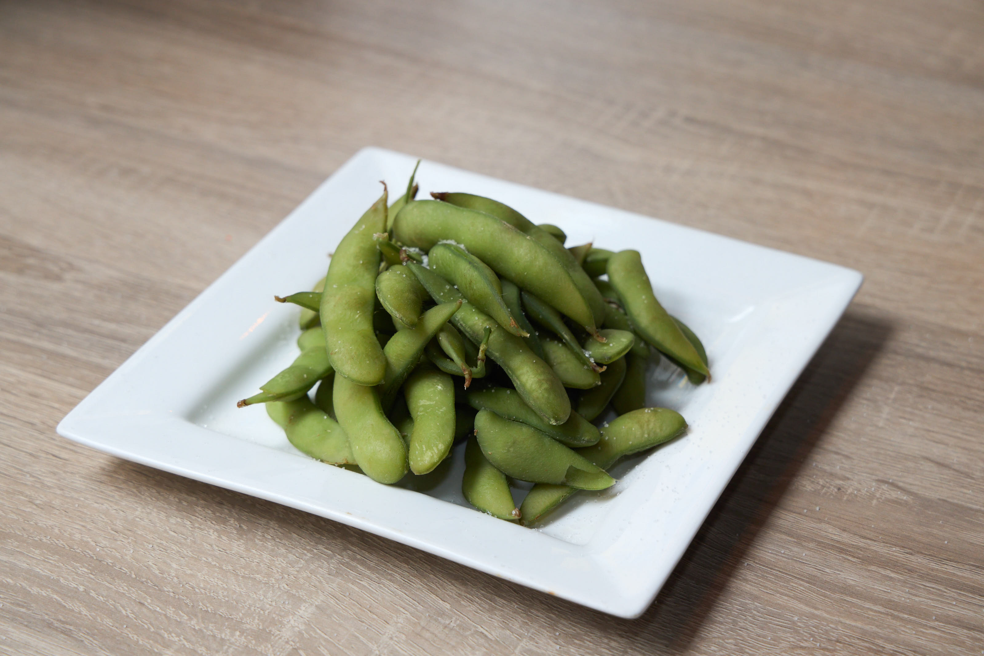 Salted edamame pods on a white square plate