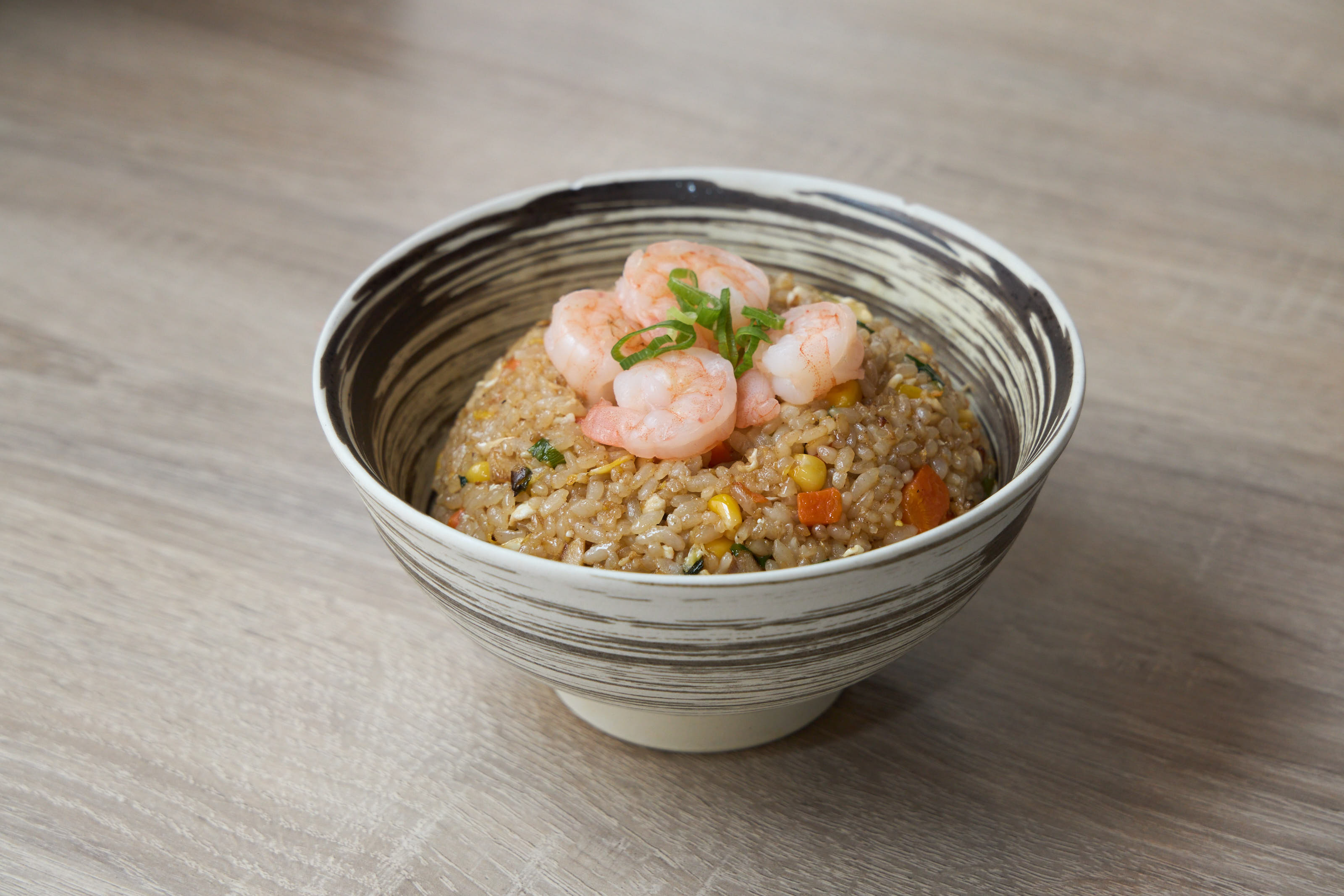 Shrimp fried rice with vegetables topped with fresh shrimp in a bowl