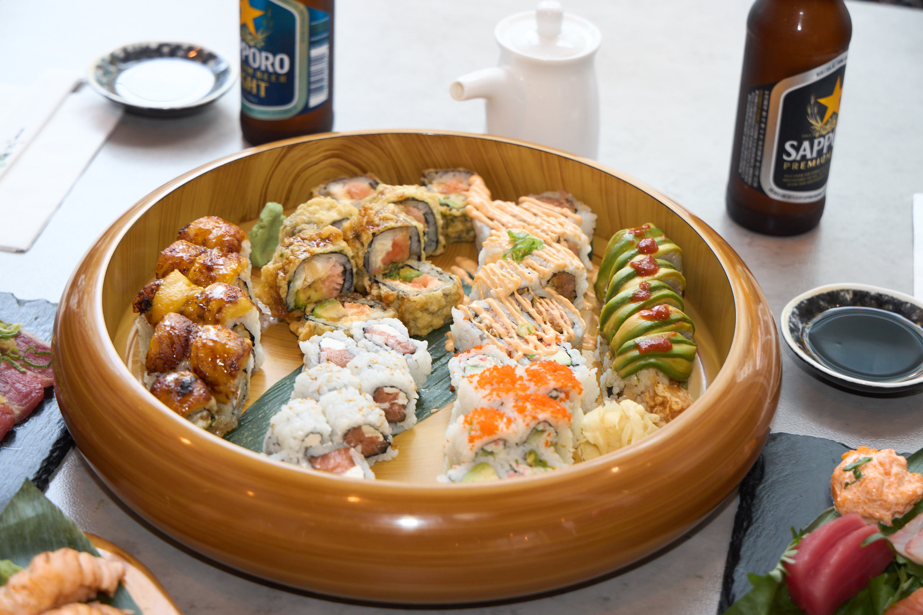 Large gold round platter filled with assorted specialty rolls including baked, tempura, and mango rolls