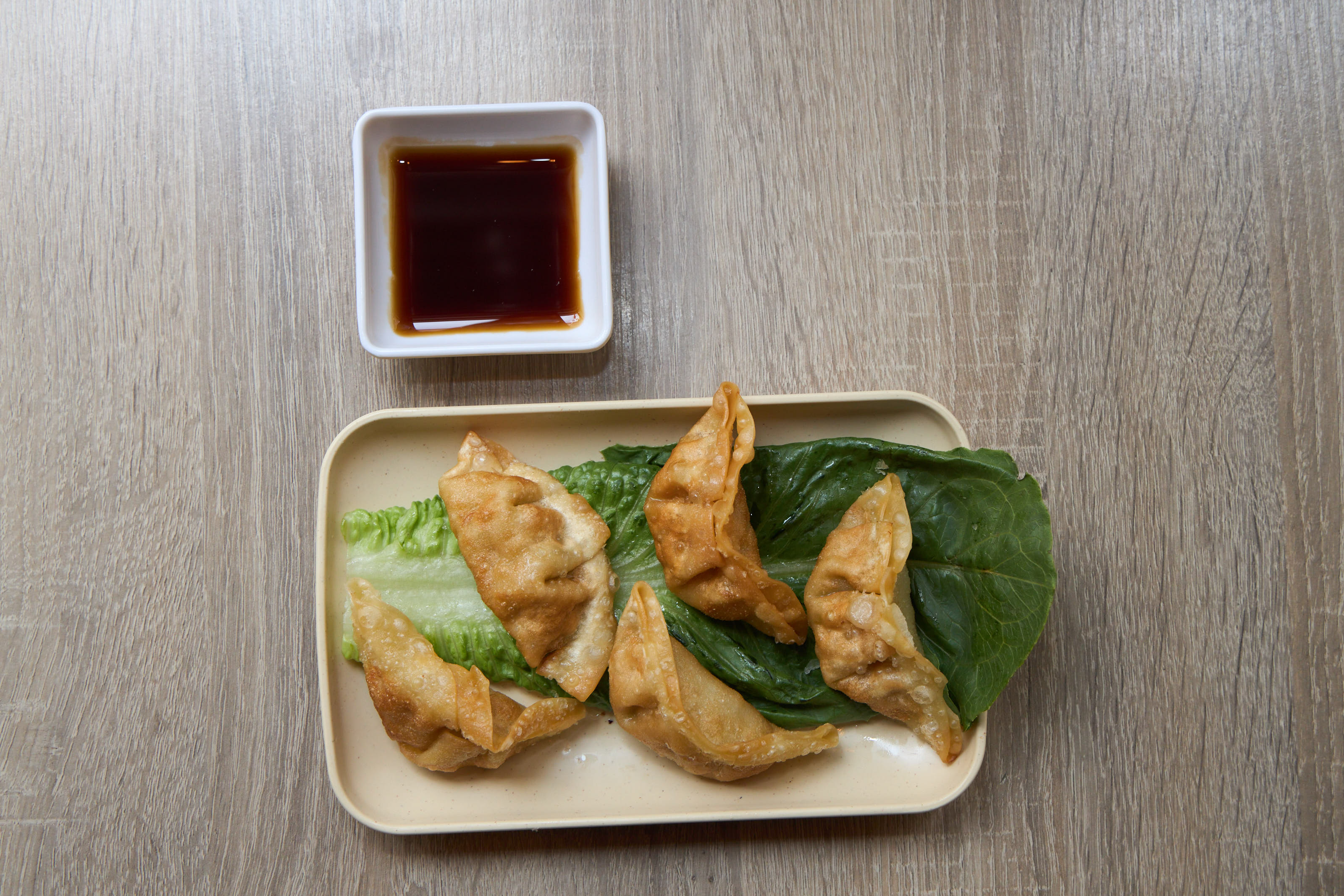 Crispy fried gyoza dumplings on lettuce with soy dipping sauce