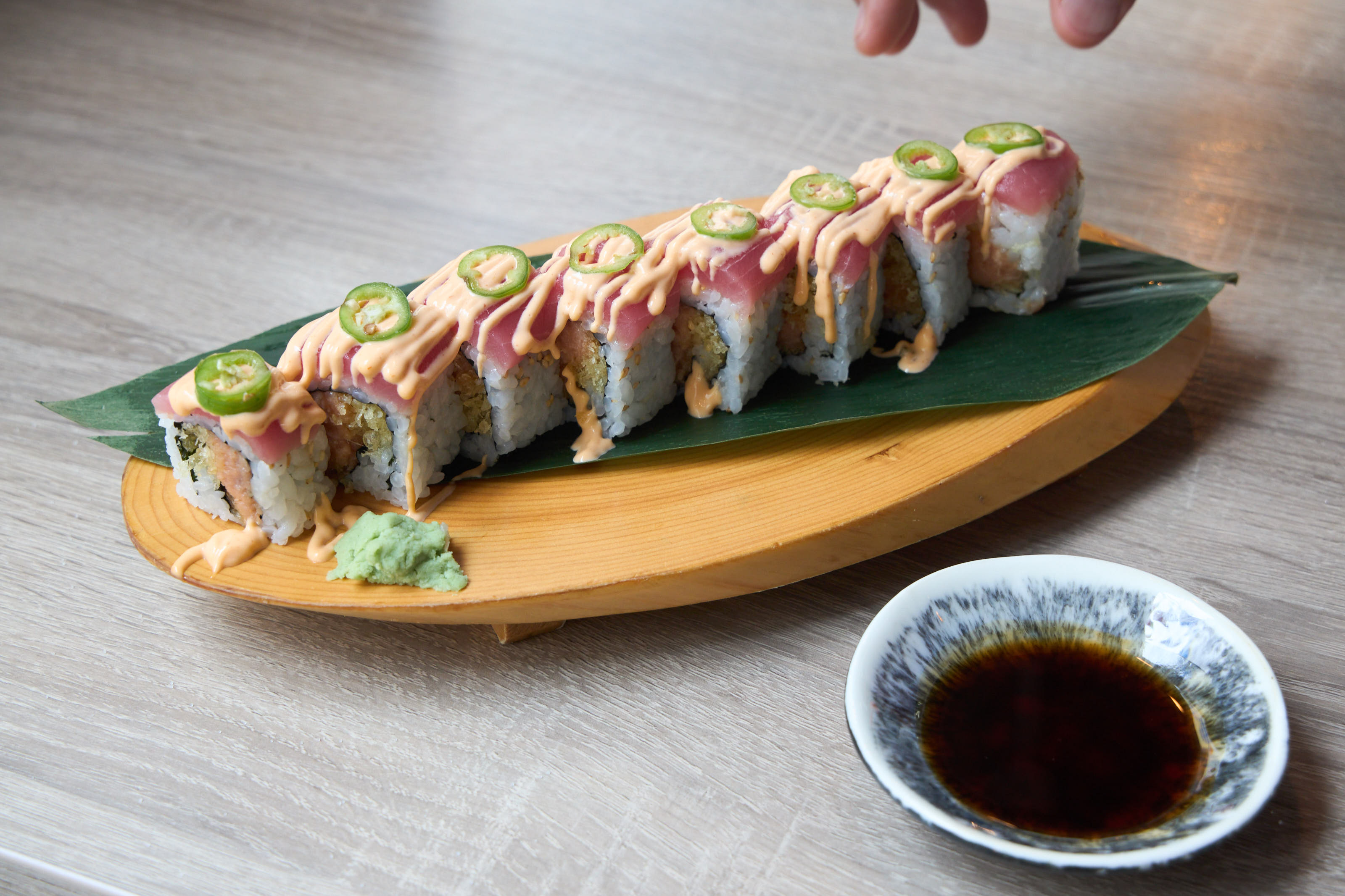 Jalapeño tuna roll with spicy mayo and jalapeño slices on wood board