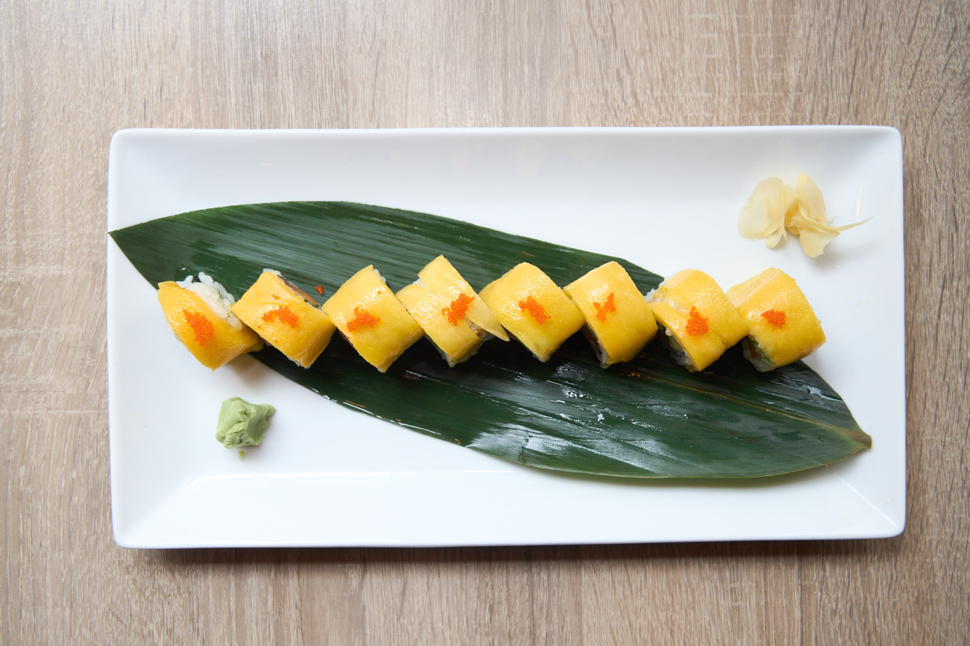 Mango roll with tobiko arranged on a banana leaf overhead