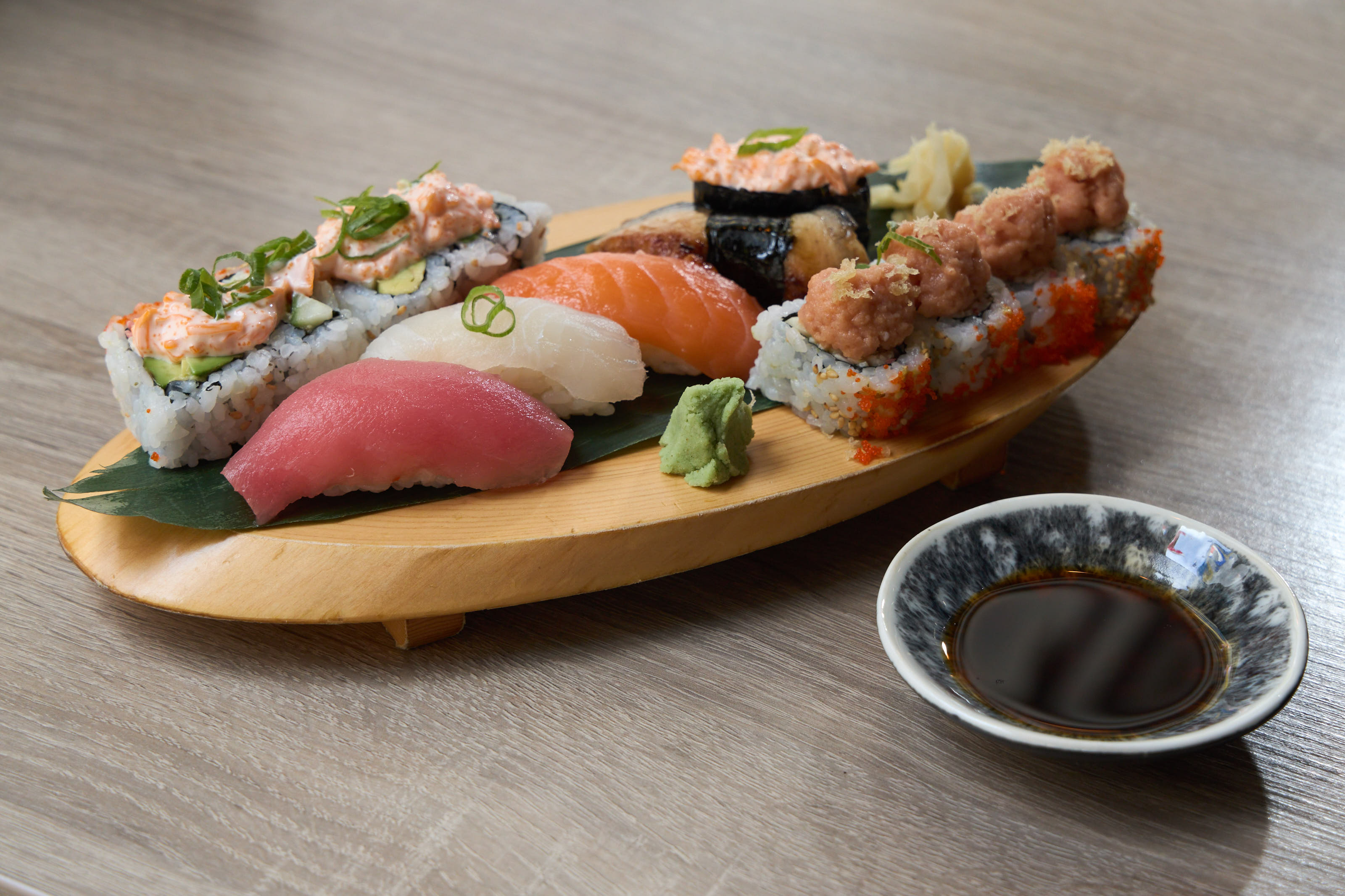 Assorted nigiri and rolls on a wooden boat with soy sauce