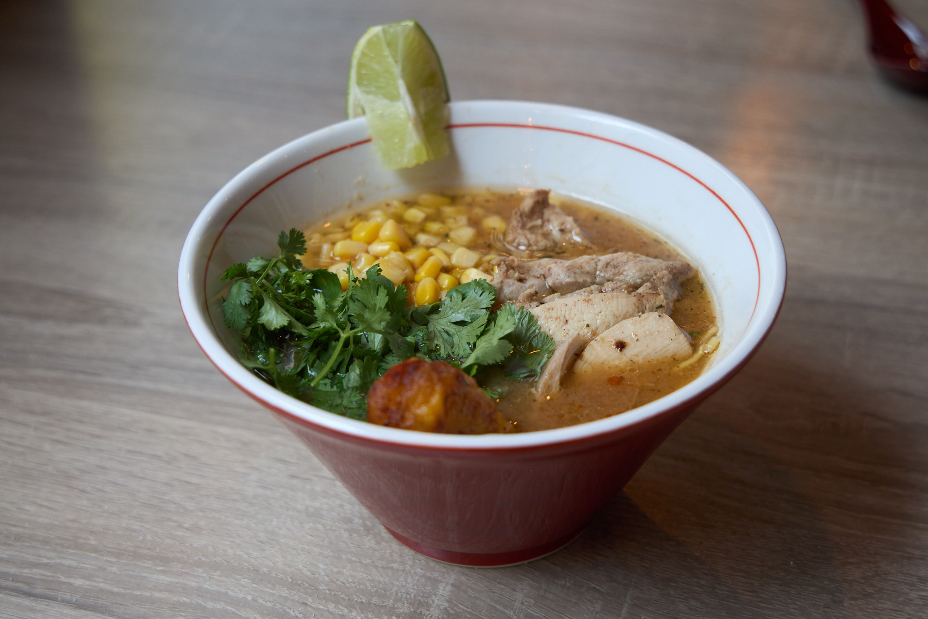 Chicken ramen with corn, cilantro, and lime in red and white bowl