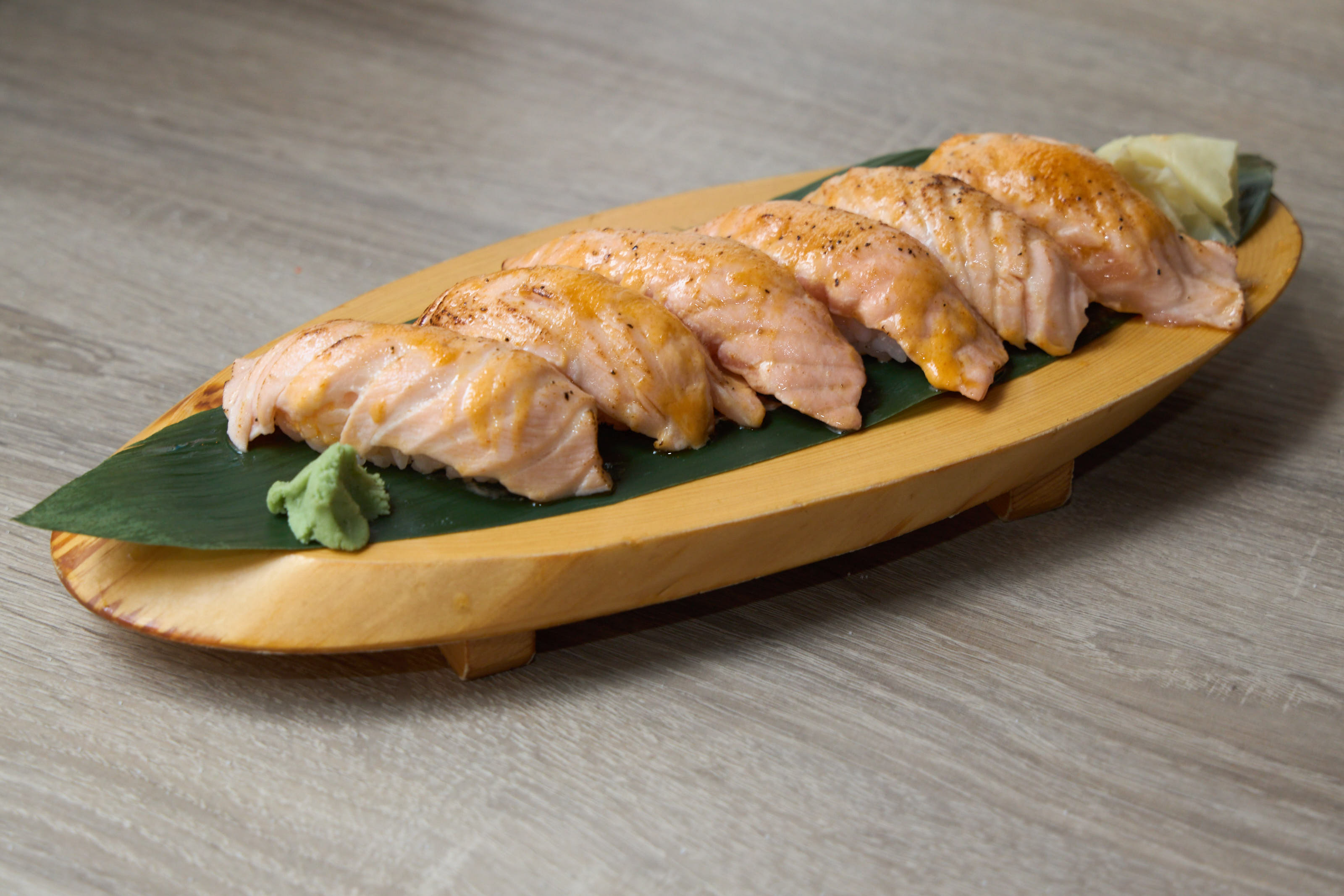 Row of seared salmon nigiri on wooden oval boat with banana leaf