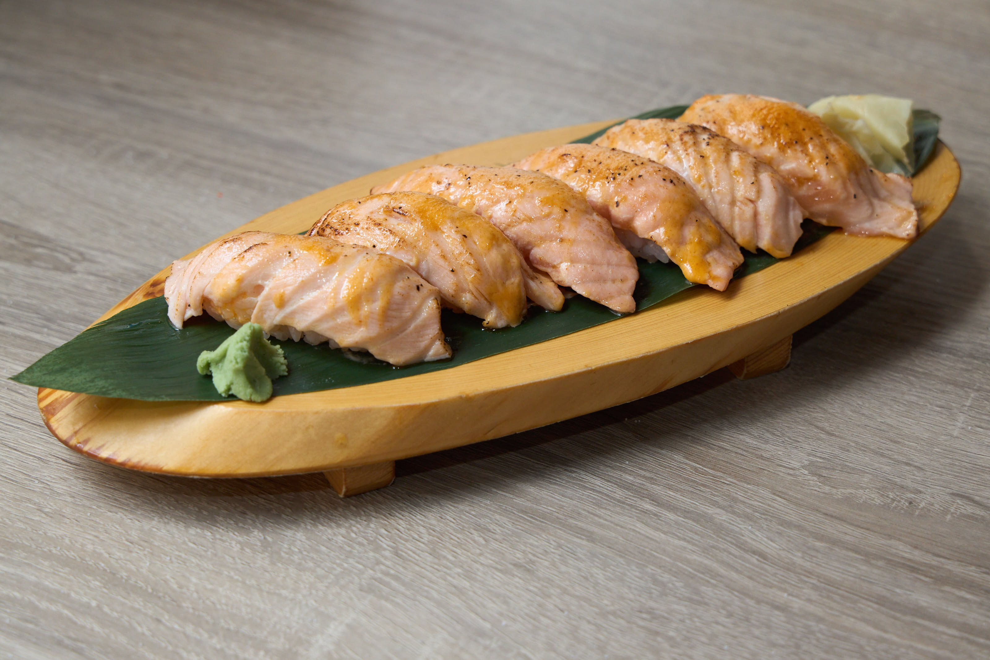 Seared salmon nigiri lined up on wood board with banana leaf