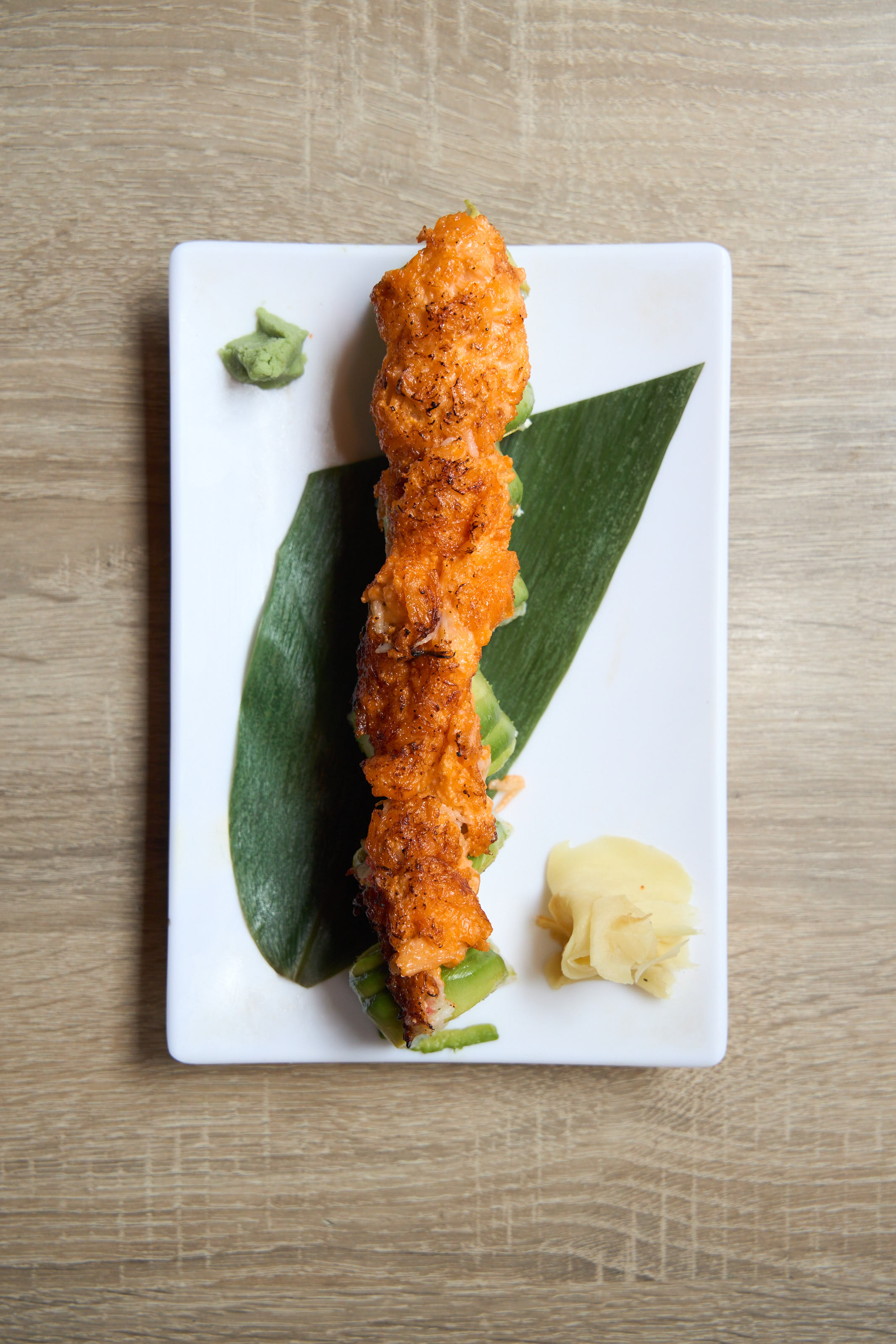 Spicy salmon roll overhead on white rectangular plate with banana leaf