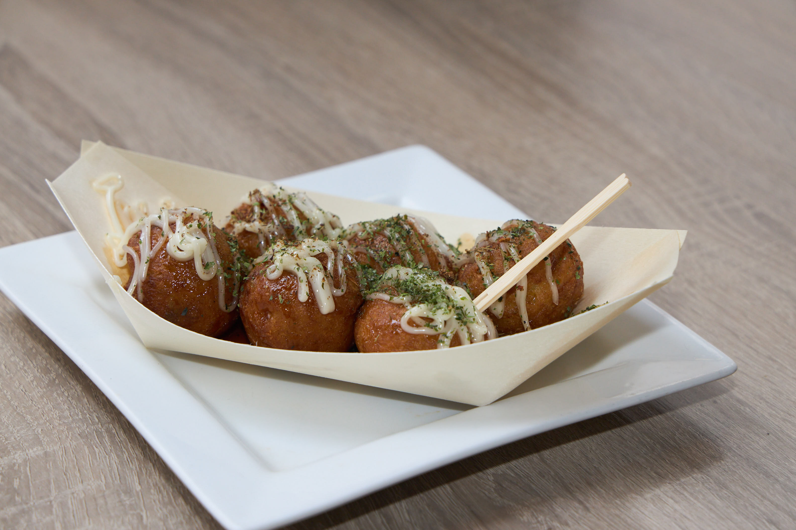 Crispy takoyaki balls in a paper boat with chopsticks