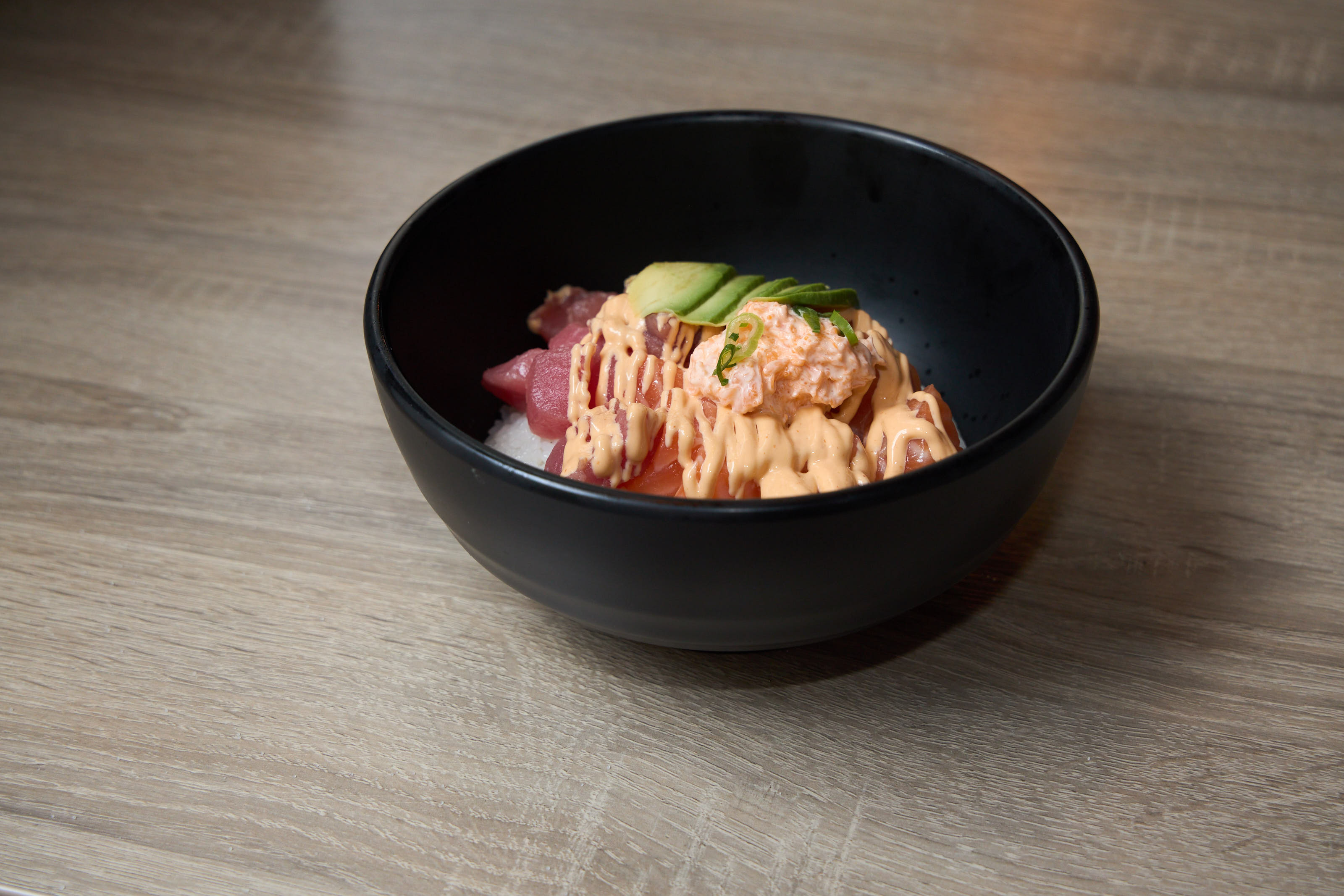Tuna and salmon poke bowl with avocado and spicy mayo in black bowl