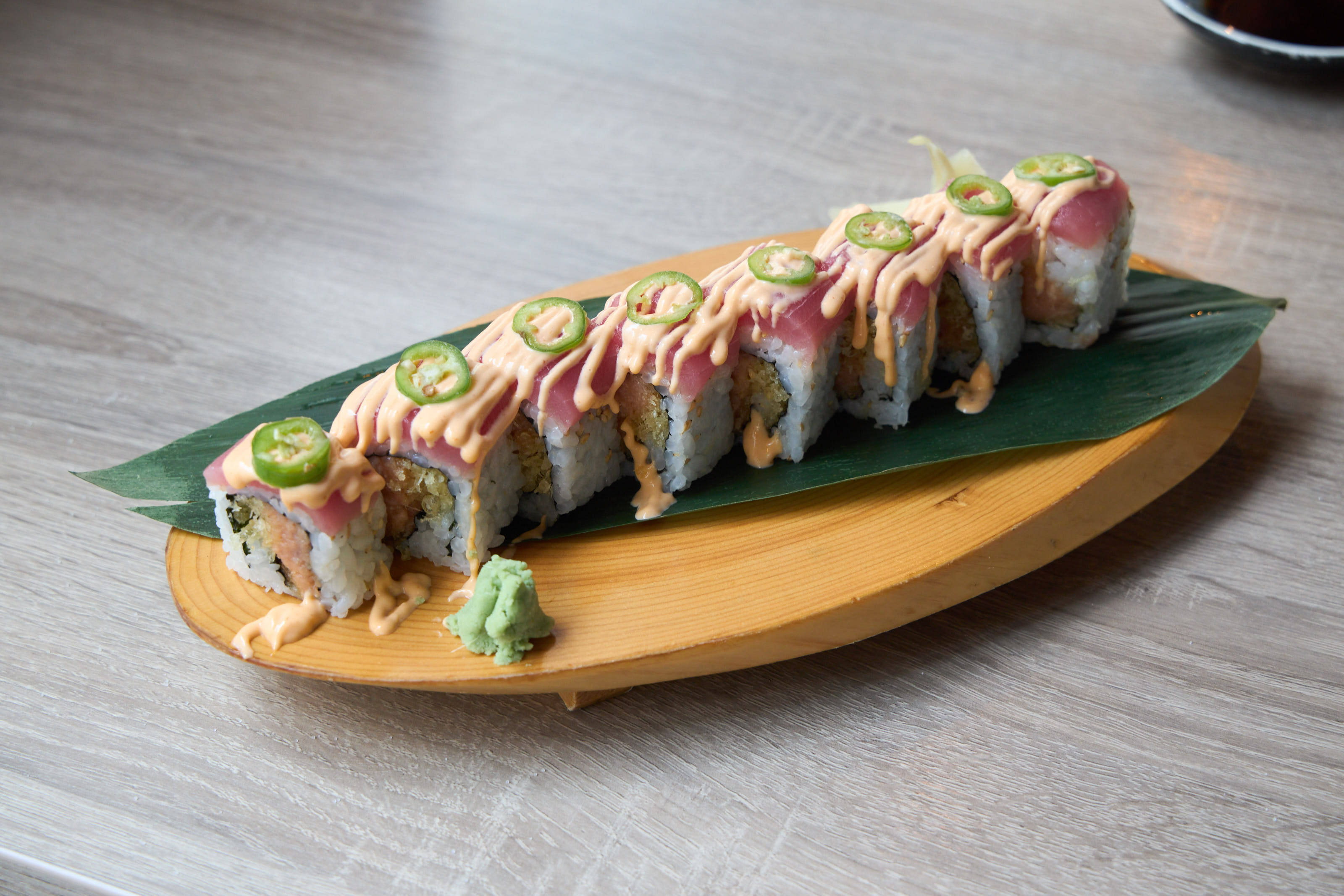 Jalapeño tuna roll with tuna cap, jalapeño slices and spicy mayo on wooden boat